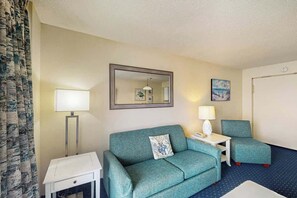 A hotel room with a sofa, a chair, a bedside table, a lamp, and a mirror. - Bay Watch Resort 1114 (North Myrtle Beach)