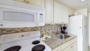 A kitchen with white cabinets, a microwave, a stove, a sink, and a refrigerator. - Bay Watch Resort 1135 (North Myrtle Beach)