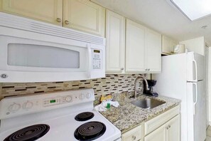 A kitchen with white cabinets, a microwave, a stove, a sink, and a refrigerator. - Bay Watch Resort 1135 (North Myrtle Beach)