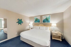 A hotel room with a large bed, two bedside tables, a nightstand, and artwork on the walls. - Bay Watch Resort 1131 (North Myrtle Beach)