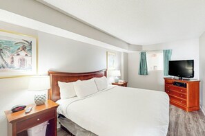 Een hotelkamer met een groot bed, een televisie, een nachtkastje met een lamp en een schilderij aan de muur.
