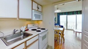 A kitchen with a microwave, stove, and sink. There is a dining area with a table and chairs. - Bay Watch Resort 1139 (North Myrtle Beach)