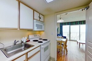 A kitchen with a microwave, stove, and sink. There is a dining area with a table and chairs. - Bay Watch Resort 1139 (North Myrtle Beach)