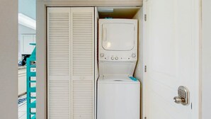 A laundry room with a washing machine and dryer, a teal chair, and a white door with a keypad lock. - Bay Watch Resort 1422 (North Myrtle Beach)