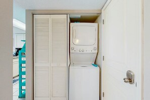 A laundry room with a washing machine and dryer, a teal chair, and a white door with a keypad lock. - Bay Watch Resort 1422 (North Myrtle Beach)