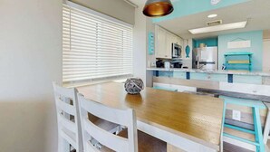 A dining area with a wooden table, white chairs, and a pendant light. - Bay Watch Resort 1422 (North Myrtle Beach)