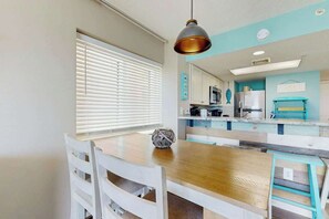 A dining area with a wooden table, white chairs, and a pendant light. - Bay Watch Resort 1422 (North Myrtle Beach)