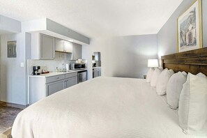 A hotel room with a large bed, a wooden headboard, a kitchen area, and a painting on the wall. - Bay Watch Resort 1431 (North Myrtle Beach)