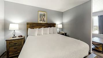Une chambre d’hôtel avec un grand lit, deux tables de chevet, une petite table, un tableau encadré au mur et une fenêtre avec des rideaux.
