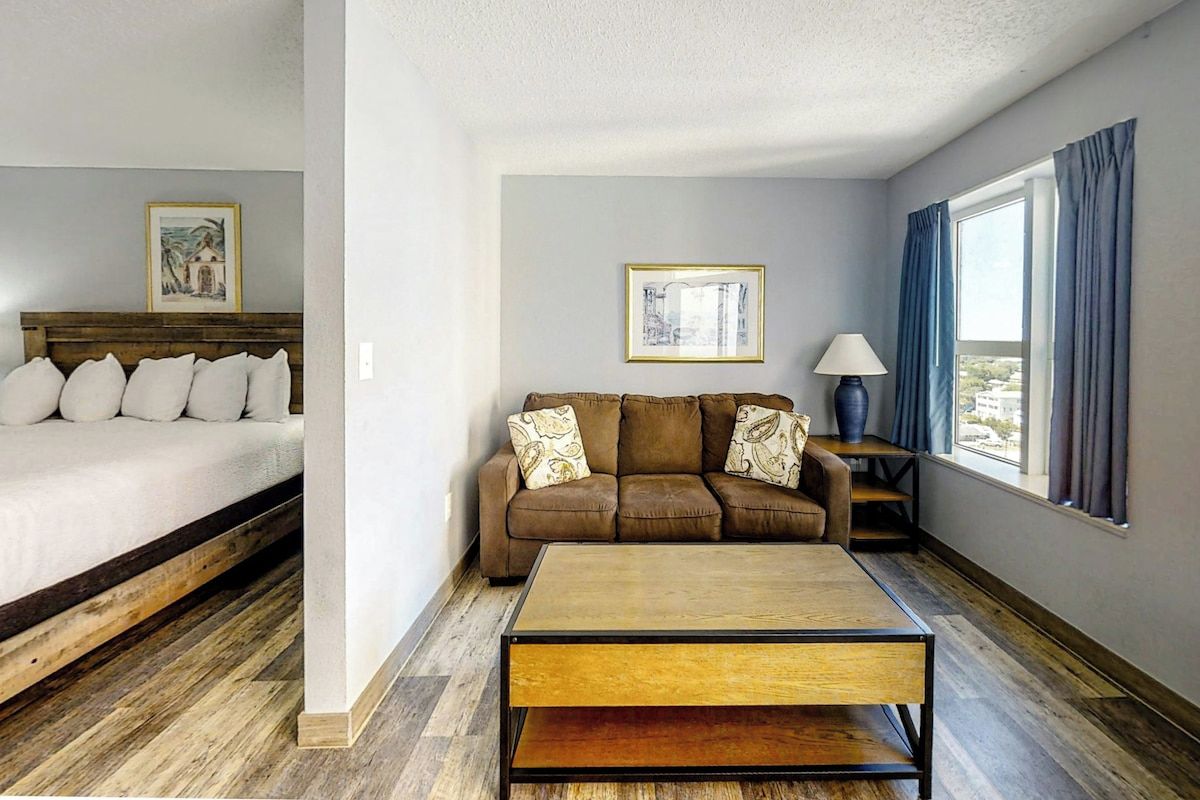 A hotel room with a bed, a sofa, a coffee table, and a window with curtains.
