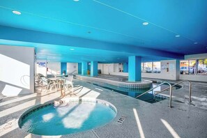 An indoor swimming pool with a blue ceiling, clear water, and a sunlit area with a table and chairs. - Bay Watch Resort 1431 (North Myrtle Beach)