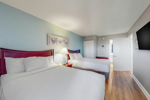 A hotel room with two beds, a nightstand with a lamp, a wall-mounted artwork, and a door leading to another room. - Bay Watch Resort 1215 (North Myrtle Beach)