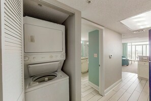 Une buanderie équipée d’un lave-linge et d’un sèche-linge à chargement frontal, une porte donnant accès à une salle de bain et un sol carrelé.