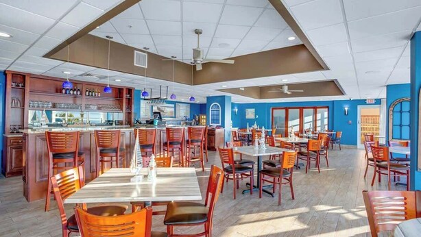 Um restaurante amplo com várias mesas e cadeiras, um espaço de bar e um ventilador de teto.