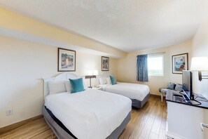 Ein Hotelzimmer mit zwei Betten, einem Schreibtisch mit Computer und einem Fenster mit Vorhängen.