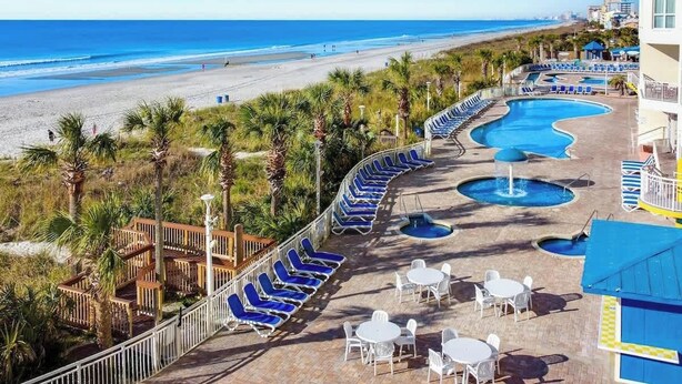 Een resort met een zwembad, ligbedden en uitzicht op het strand.