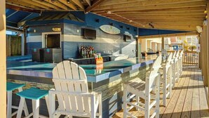 Een buitengebied met een bar, een zwembad en houten terras met barstoelen.
