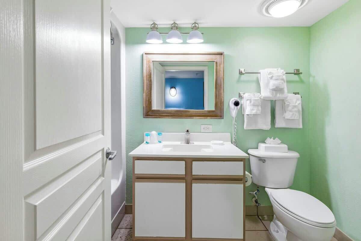 A bathroom with a white sink, a mirror, a toilet, and a towel rack with towels.