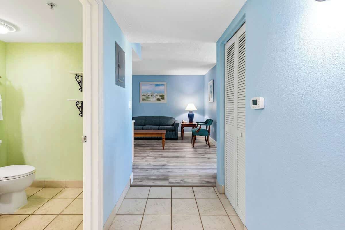 Corredor que leva a uma sala de estar com um sofá, uma luminária e uma poltrona.