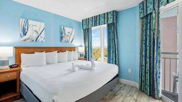A hotel room with a large bed, a wooden headboard, a nightstand, a window with curtains, and artwork on the walls.