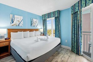 Ein Hotelzimmer mit einem großen Bett, einem Holzkopfende, einem Nachttisch, einem Fenster mit Vorhängen und Bildern an den Wänden.