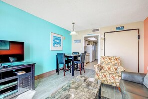 Ein Wohnzimmer mit Fernseher, Esstisch mit Stühlen, einem gemusterten Sessel und einer Couch.