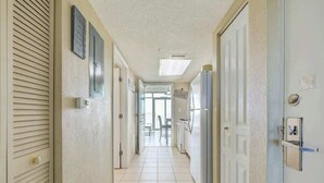 Um corredor com piso ladrilhado, uma porta com puxador, um termostato fixado na parede e uma placa com a palavra 'CUCINA'.