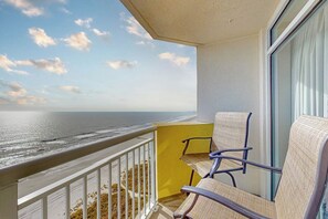Un balcon avec vue sur l’océan, deux chaises et un mur jaune.