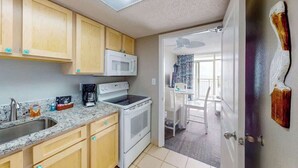 A compact kitchen with wooden cabinets, a microwave, a stove, and a sink. - Bay Watch Resort 1407 (North Myrtle Beach)