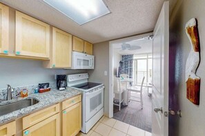 A compact kitchen with wooden cabinets, a microwave, a stove, and a sink. - Bay Watch Resort 1407 (North Myrtle Beach)