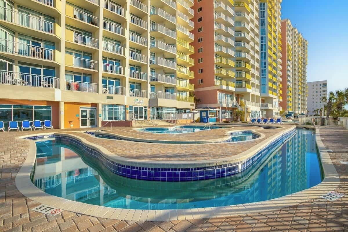 Ein Hotel mit mehreren Etagen, einem Außenpool und blauen Stühlen.