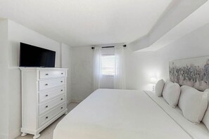 A bedroom with a bed, a dresser, a flat-screen TV, a window with curtains, and a painting on the wall. - Bay Watch Resort 1408 (North Myrtle Beach)