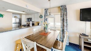 Una cocina moderna con electrodomésticos de acero inoxidable, una zona de comedor con mesa y sillas de madera, y un televisor de pantalla plana en la pared.