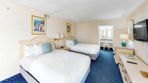 Habitación de hotel con dos camas, un escritorio, un televisor y obras de arte en las paredes.