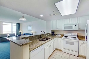 A modern kitchen with white cabinets, a granite countertop, a built-in microwave, and a stove. - Bay Watch Resort 1412 (North Myrtle Beach)