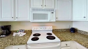 A kitchen with white cabinets, a microwave, a stove, and granite countertops. - Bay Watch Resort 1412 (North Myrtle Beach)