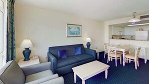 A living room with a sofa, a coffee table, and a dining area with chairs and a table. - Bay Watch Resort 1412 (North Myrtle Beach)