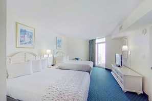 Une chambre d’hôtel avec deux lits, une commode, un téléviseur et des œuvres d’art accrochées aux murs.