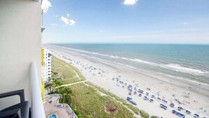 A balcony overlooking a beach with a view of the ocean and a parking area with several cars. - Bay Watch Resort 1414 (North Myrtle Beach)
