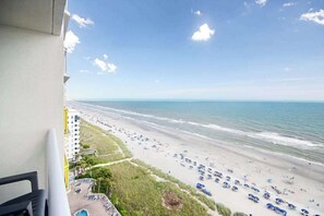 A balcony overlooking a beach with a view of the ocean and a parking area with several cars. - Bay Watch Resort 1414 (North Myrtle Beach)