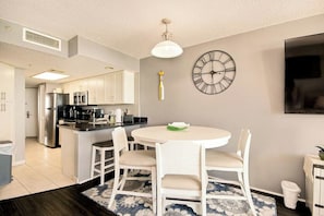 A modern kitchen with white cabinetry, a built-in island, and a round dining table with chairs. - Bay Watch Resort 1414 (North Myrtle Beach)