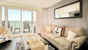 A living room with a sofa, a coffee table, and a balcony with chairs. - Bay Watch Resort 1414 (North Myrtle Beach)