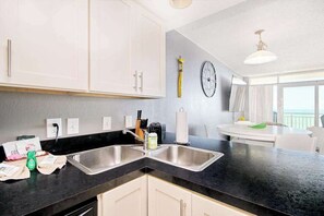A modern kitchen with two sinks, a black countertop, and white cabinets. There is a window with a view of the ocean. - Bay Watch Resort 1414 (North Myrtle Beach)
