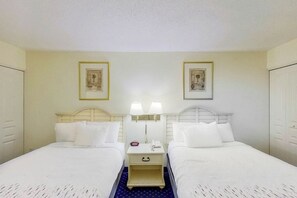 A hotel room with two single beds, a small bedside table with a lamp, a nightstand, and a framed picture on the wall. - Bay Watch Resort 1417 (North Myrtle Beach)