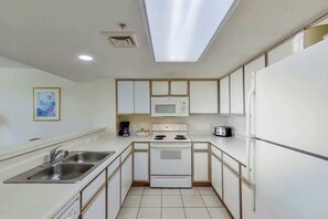 A compact kitchen with white cabinets, a microwave, a stove, a sink, and a refrigerator.