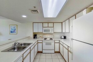A compact kitchen with white cabinets, a microwave, a stove, a sink, and a refrigerator. - Bay Watch Resort 1417 (North Myrtle Beach)