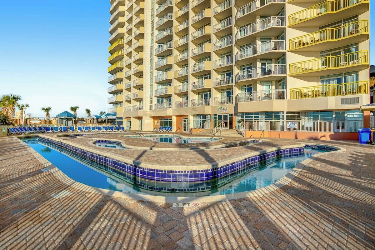 A hotel with a swimming pool, multiple balconies, and a brick-paved area.