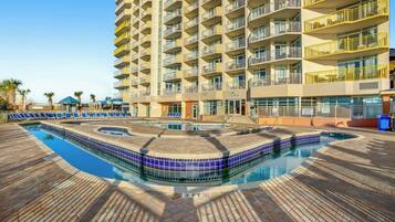 A hotel with a swimming pool, multiple balconies, and a brick-paved area.