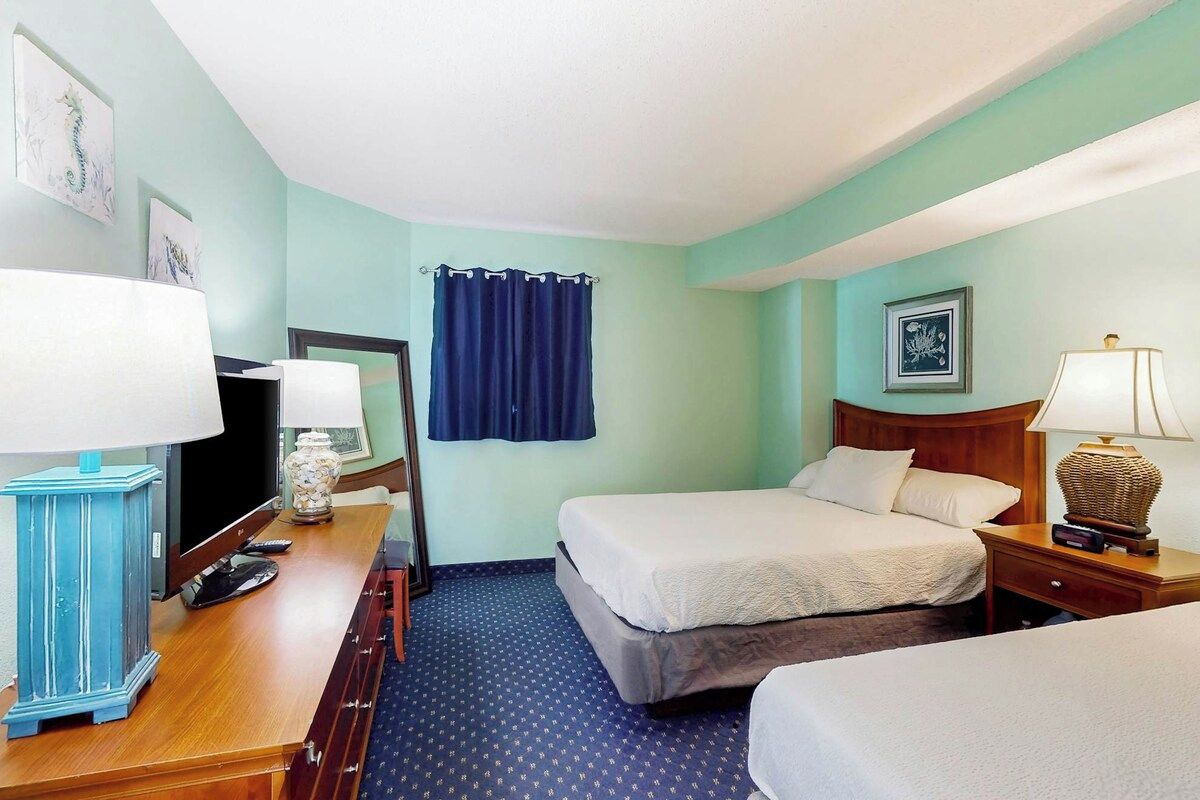 A hotel room with two beds, a desk with a computer, a lamp, and a TV.