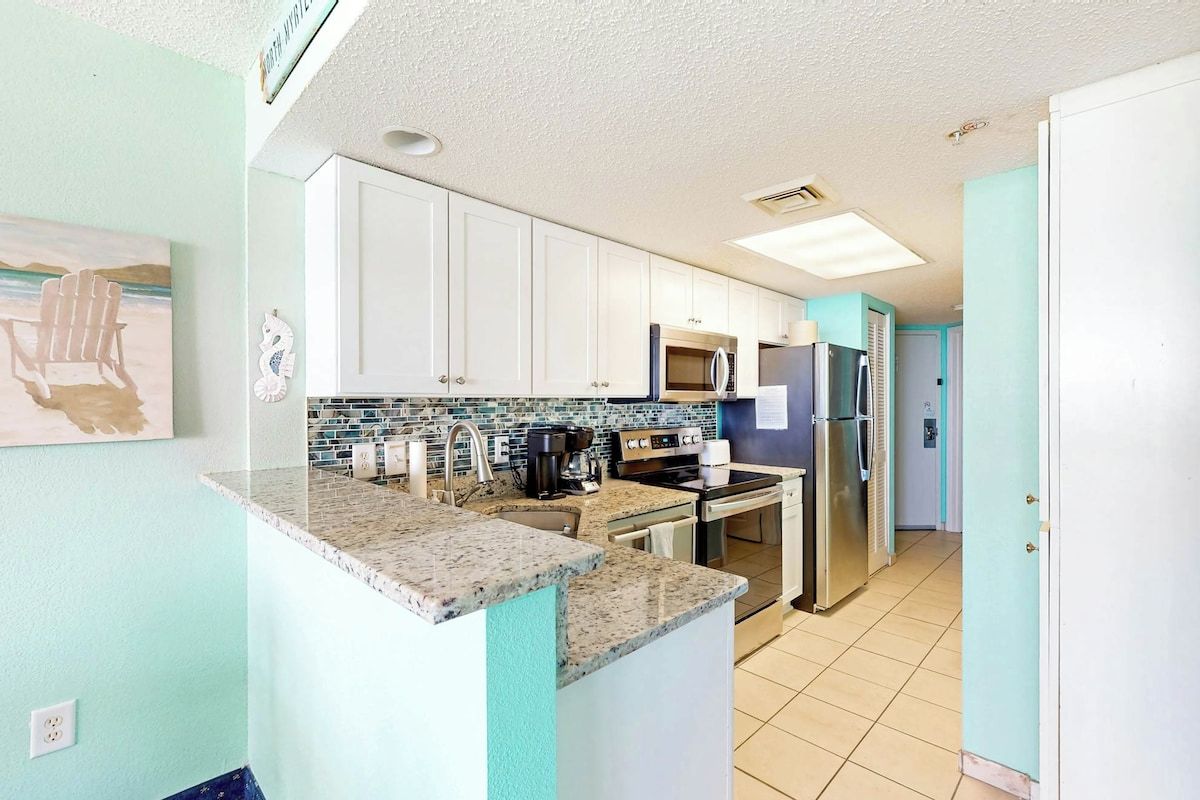 A kitchen with white cabinets, a granite countertop, a microwave, a refrigerator, and a tiled backsplash.